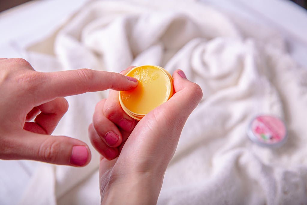 A close-up view of a hand applying lip balm on manicured fingers, emphasizing skincare and self-care.