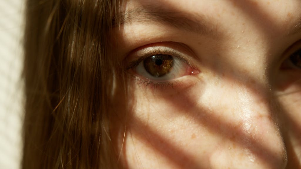 A detailed close-up of a woman's eye with sunlight casting shadows, highlighting freckles and natural features.