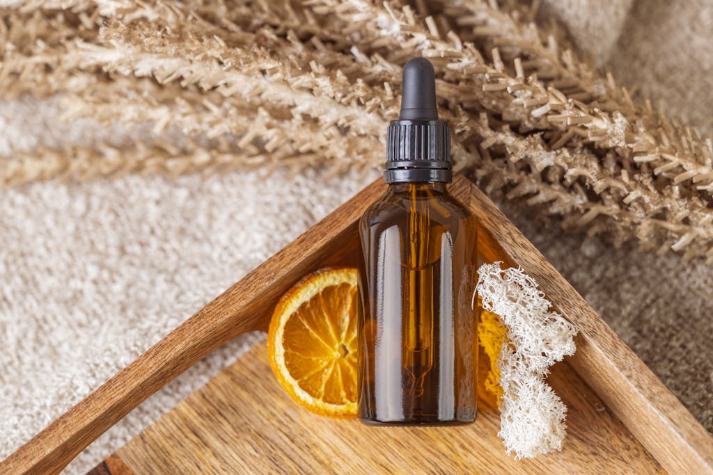 A natural face serum bottle with an orange slice on a wooden tray featuring dried botanicals.