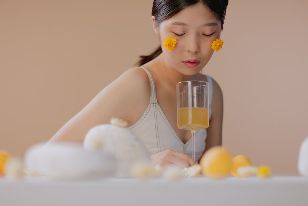 A serene portrait of a woman with flowers, eyes closed, and holding a glass of orange juice.