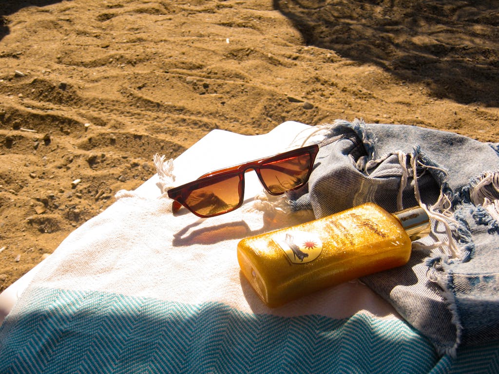A sunny beach scene with sunglasses and SPF lotion on a towel, perfect for summer travel.