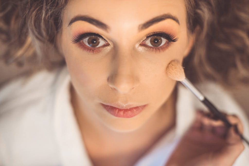 A top view of a woman applying makeup with a brush, showcasing her beautiful eyes.