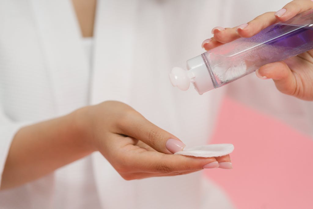 A woman applying skincare gel onto a cotton pad using a purple bottle, emphasizing body care.
