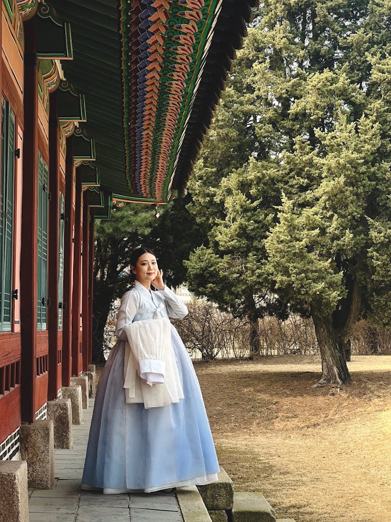 A woman in a traditional Hanbok poses in a historic Korean garden setting.