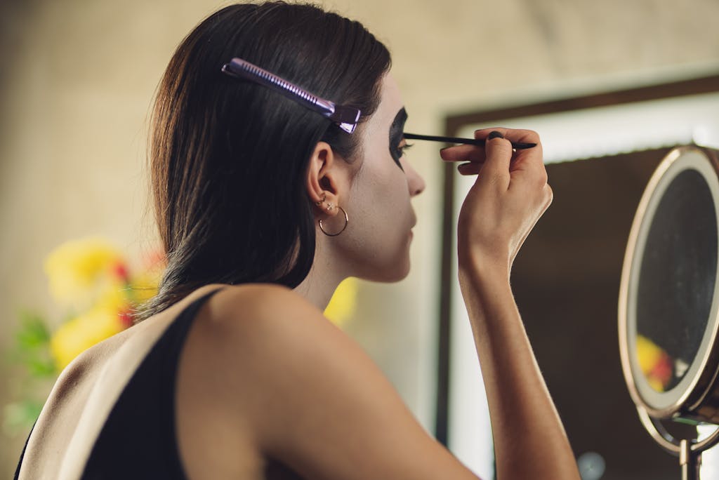 A young woman applying intricate Catrina makeup in front of a mirror with artistic focus.