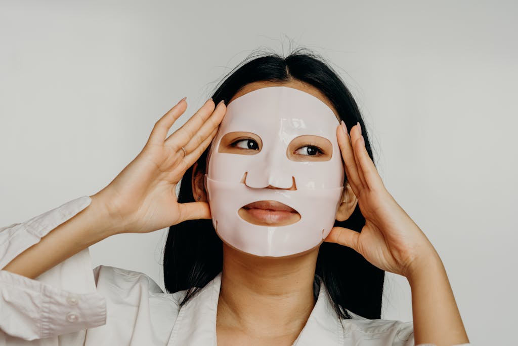 Asian woman applying hydrating sheet mask as part of her skincare routine.
