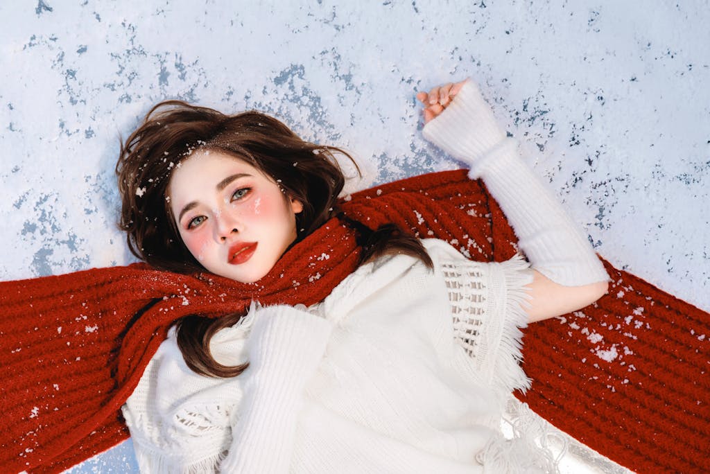 Beautiful winter portrait of a woman lying on the snow in a red scarf.