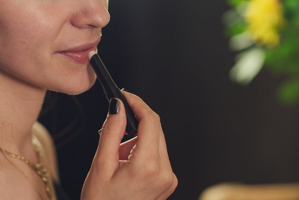 Close-up of a woman applying lipstick, featuring a blurred background for a soft focus effect.