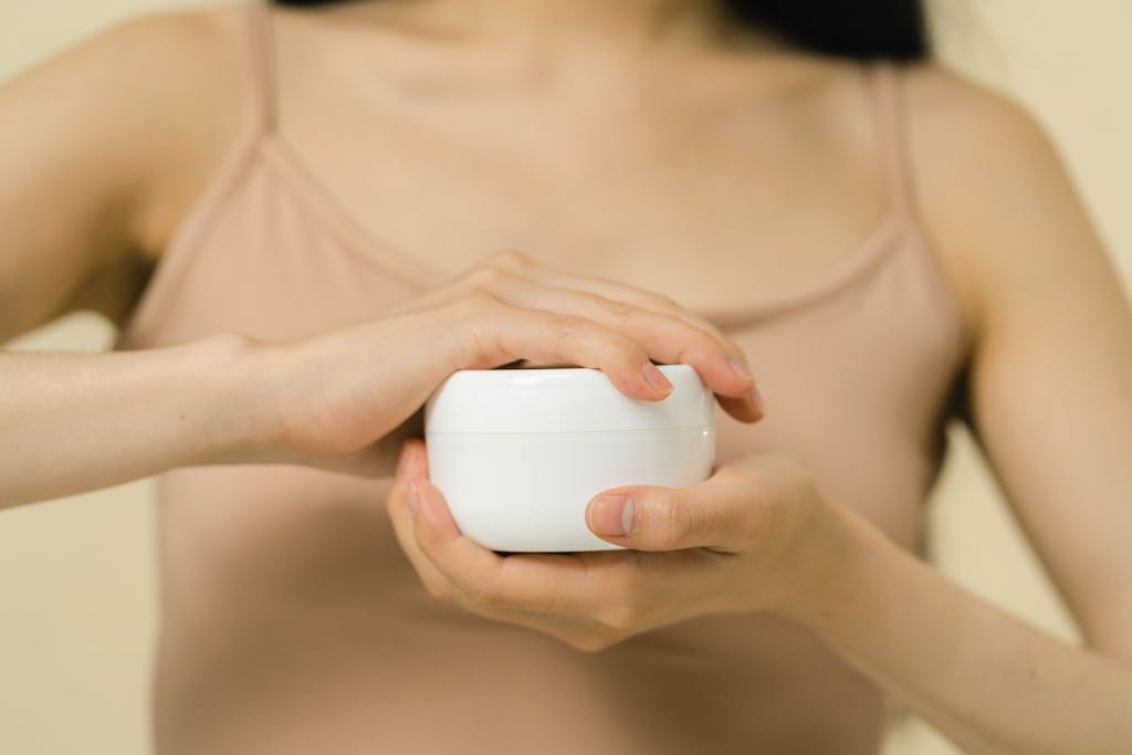 Close-up of a woman applying moisturizer with a focus on her hands and the cream container.