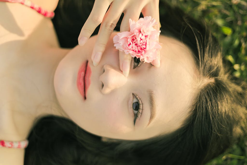 Close-up of a woman lying outdoors with a pink carnation flower, creating a serene and peaceful mood.