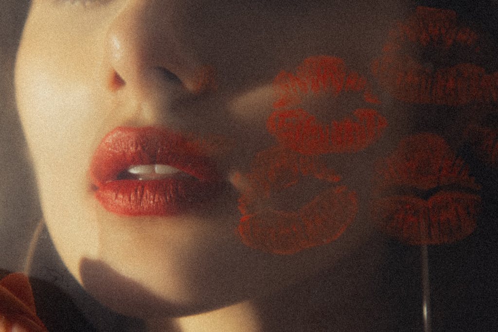 Close-up of a woman with red lips and lipstick marks under soft, artistic lighting.