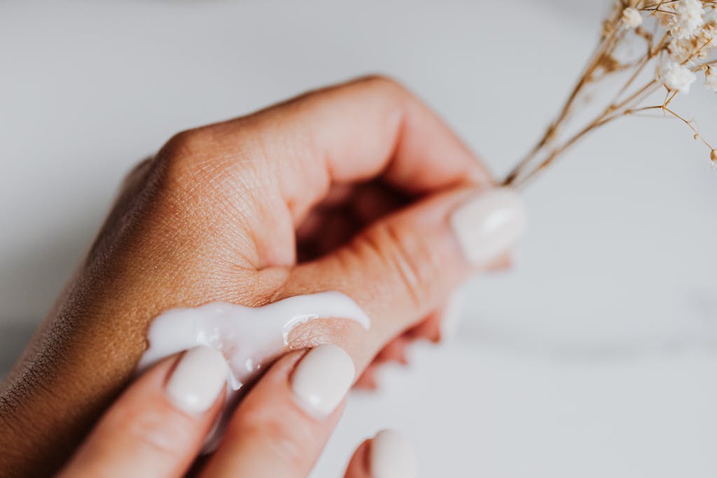 Close-up of hands applying cream, accentuated by elegant nails and dried flowers.