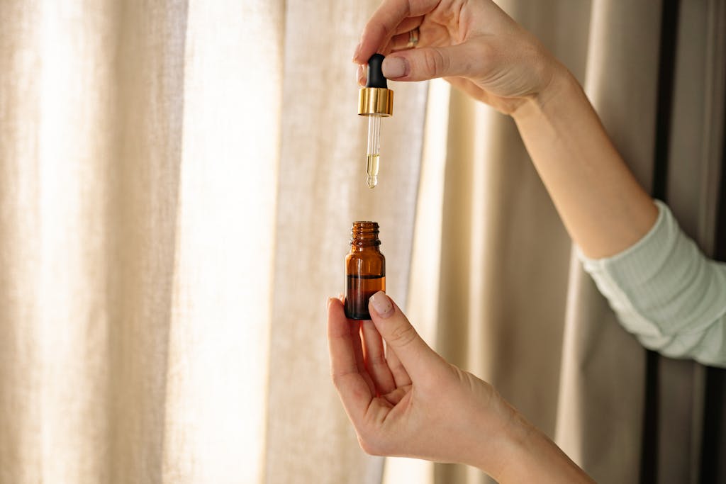Close-up of hands holding a dropper and amber bottle for skincare product.