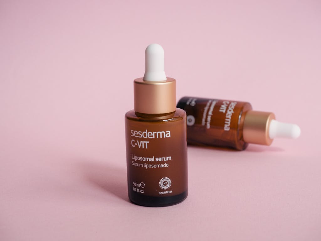 Close-up of two cosmetic serum bottles with droppers against a pink surface.