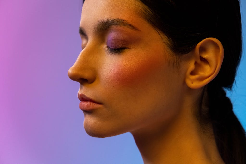 Close-up side view of a woman with vibrant blush and eye makeup in a studio setting.