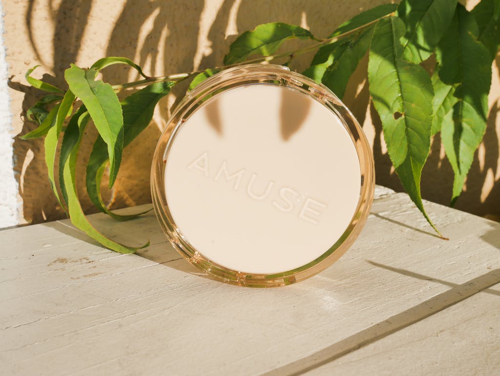 Cushion makeup compact on wooden surface with green leaves background under bright natural light.