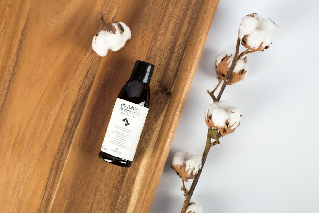 Elegant flat lay featuring treatment oil bottle and cotton on wooden surface.