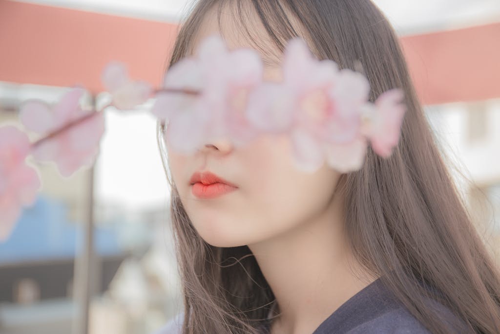 Elegant portrait featuring a soft focus on a young woman's face behind cherry blossoms, exuding serenity.