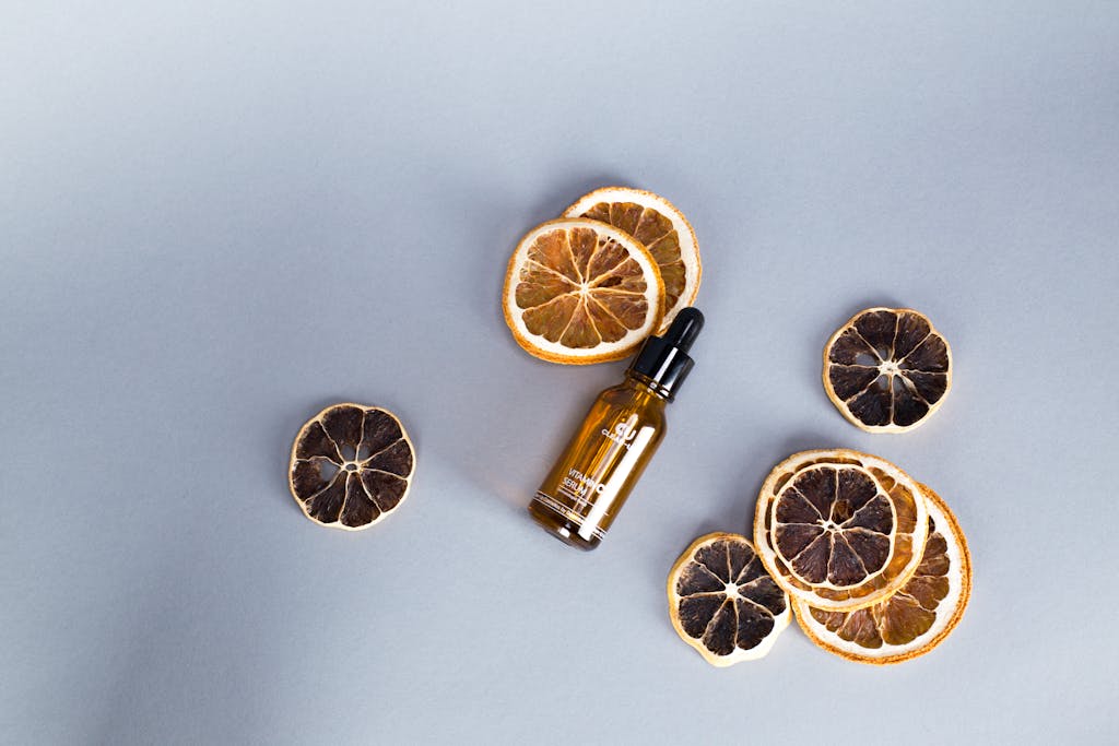 Flat lay of citrus slices and cosmetic serum bottle on gray background. Perfect for skincare and beauty themes.
