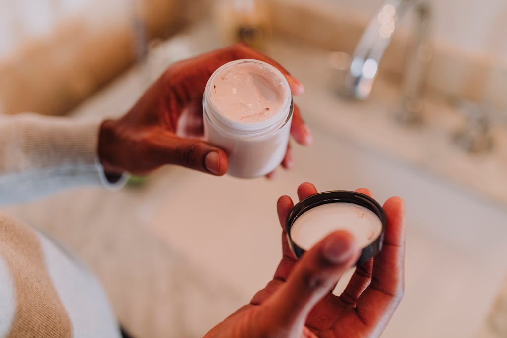 High angle view of hands holding a moisturizer jar next to a bathroom sink.