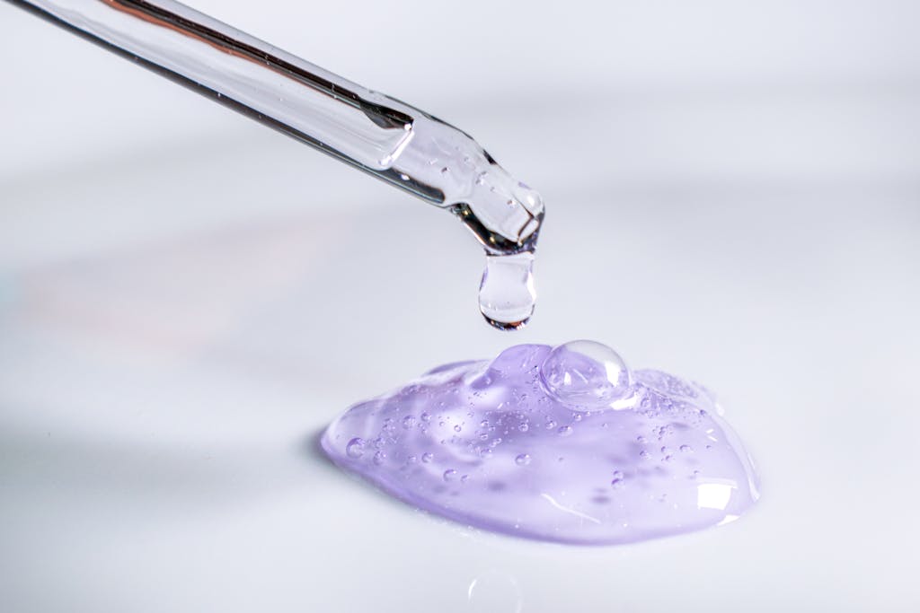 Pipette releasing drop of purple gel, highlighting skincare and laboratory use.