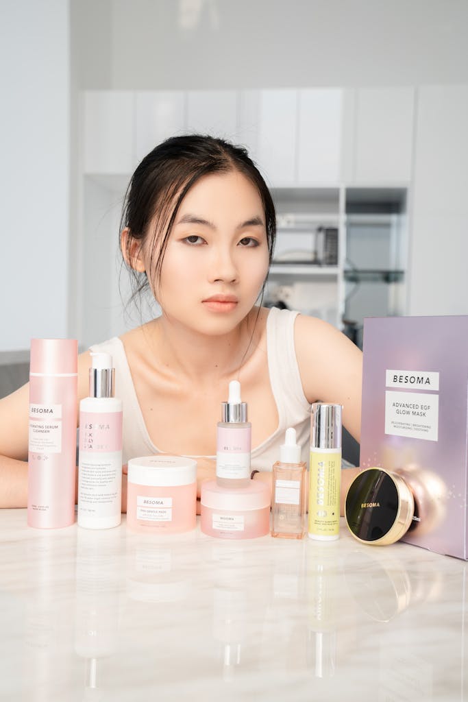 Portrait of an Asian woman with a variety of Besoma skincare products on a table.