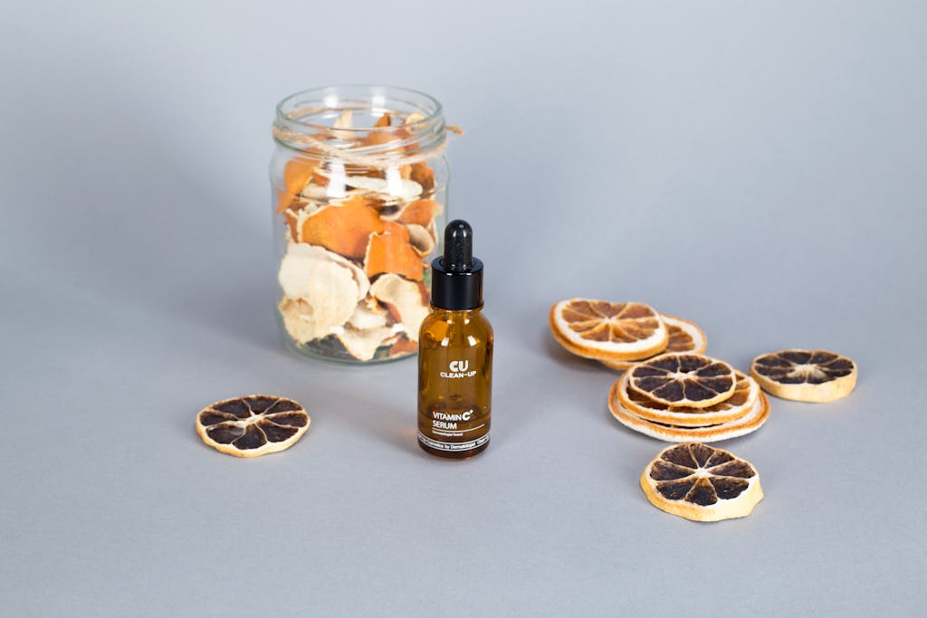 Product mockup of vitamin C serum with dried citrus slices and glass jar on a surface.
