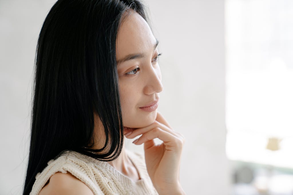 Side view of crop ethnic female with long dark hair touching chin tenderly and looking away