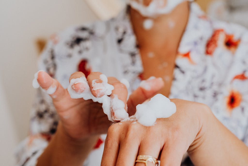 Woman in bathrobe applying facial foam for skincare routine.