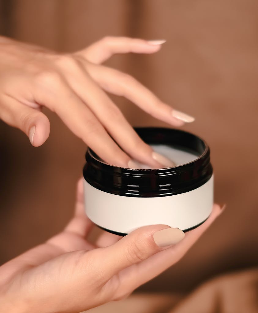 Close-up of hands applying cream from jar, symbolizing skincare and self-care.