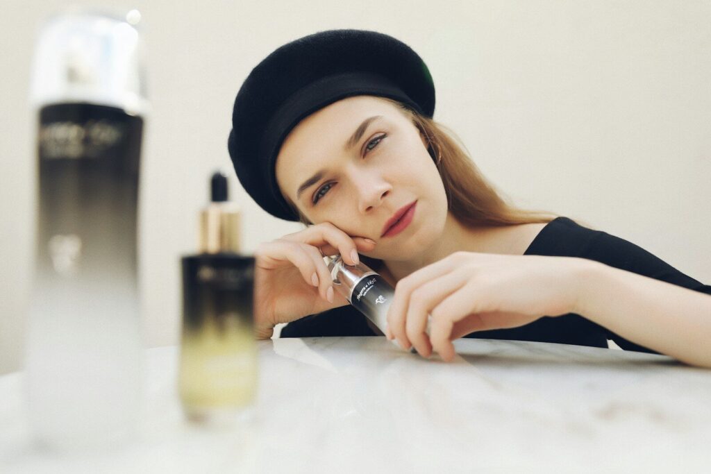 a woman sitting at a table next to a bottle of perfume