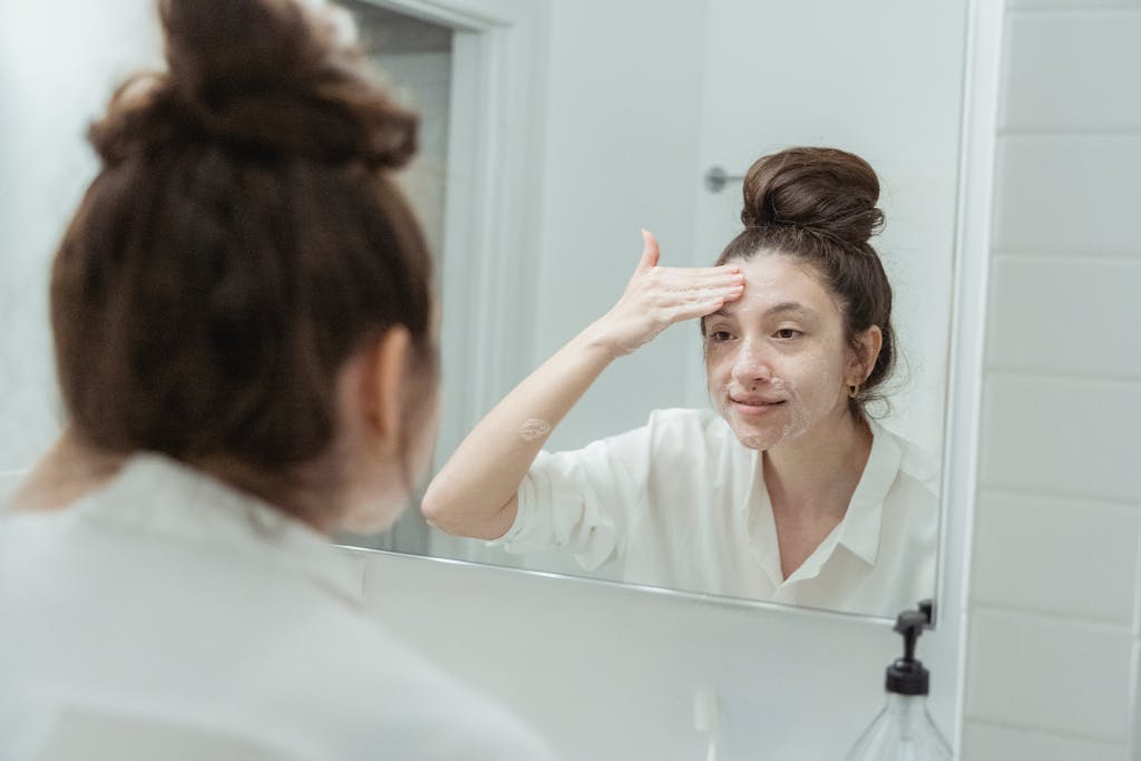 Young woman applying facial cream while looking at her reflection in the bathroom mirror.