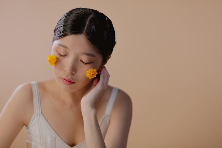 A serene portrait of a woman with yellow flowers on her cheeks, eyes closed in peaceful contemplation.