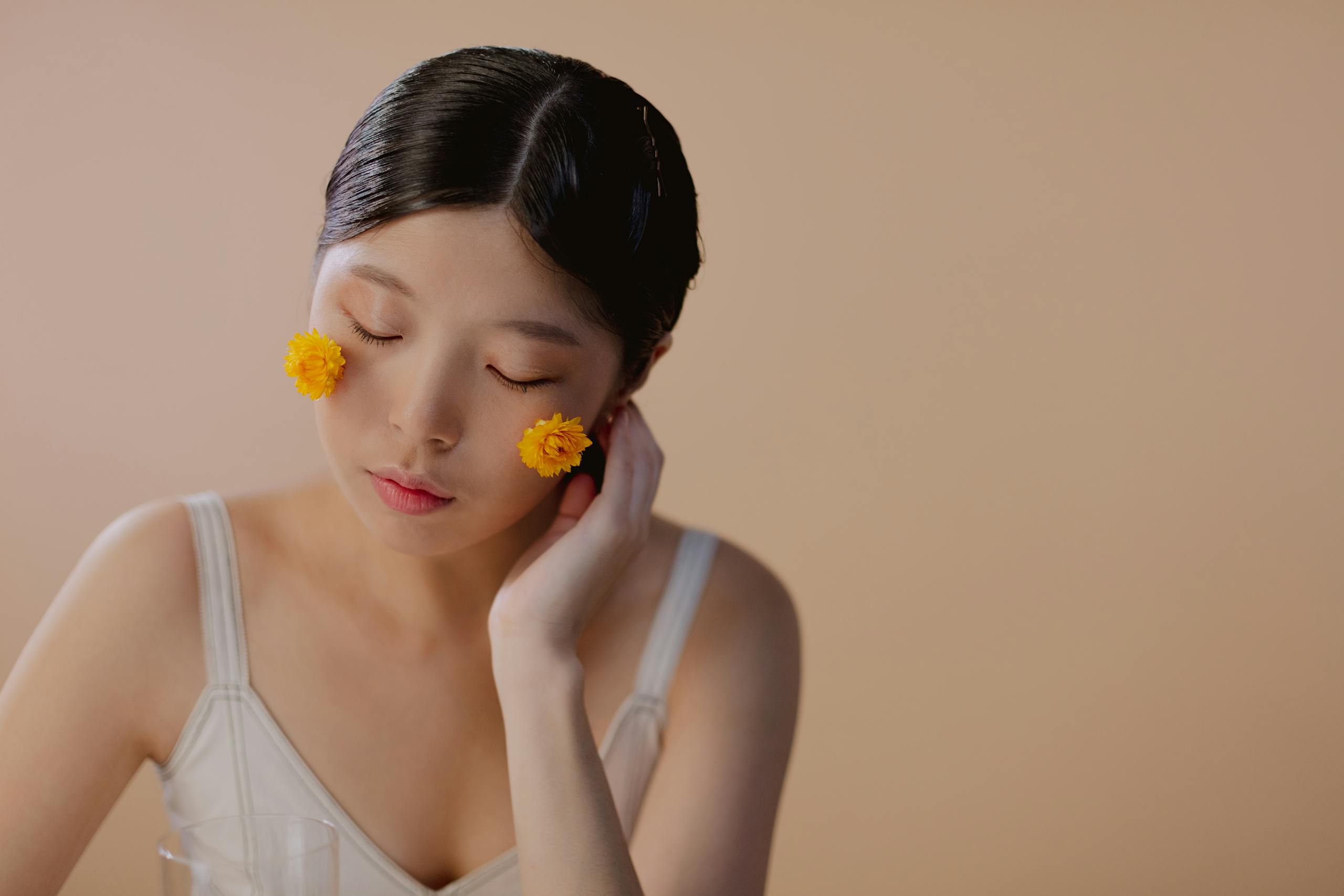 A serene portrait of a woman with yellow flowers on her cheeks, eyes closed in peaceful contemplation.