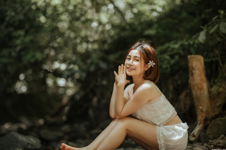 A smiling woman sitting gracefully in a tranquil forest, radiating joy and serenity.