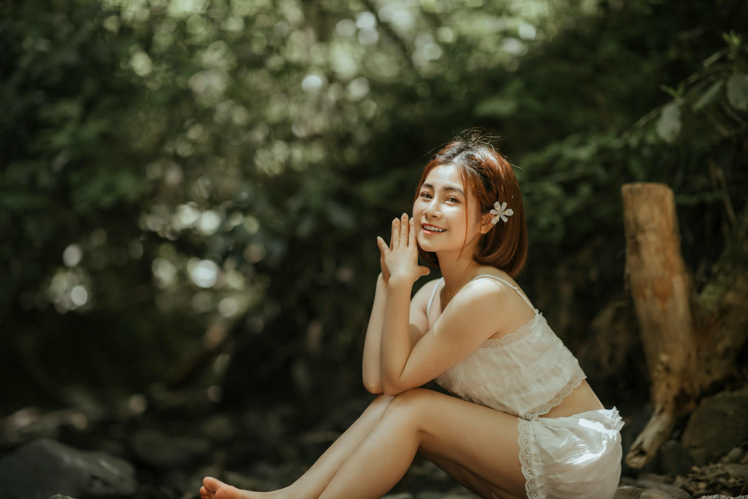 A smiling woman sitting gracefully in a tranquil forest, radiating joy and serenity.