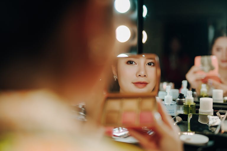 A woman applying makeup, captured in a mirror reflection surrounded by beauty products.