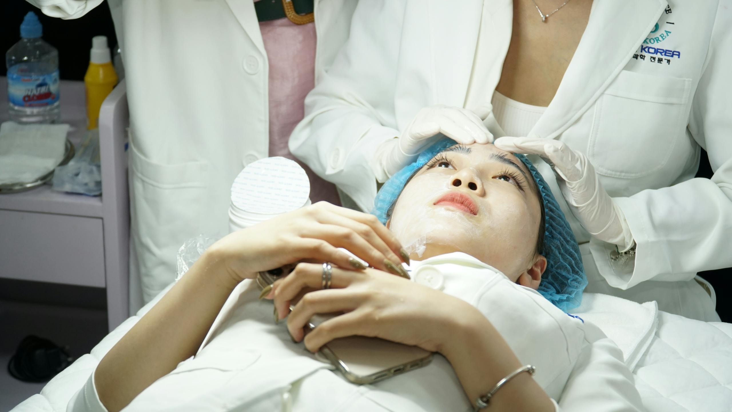 A woman receives a facial treatment at a skincare clinic, attended by specialists.