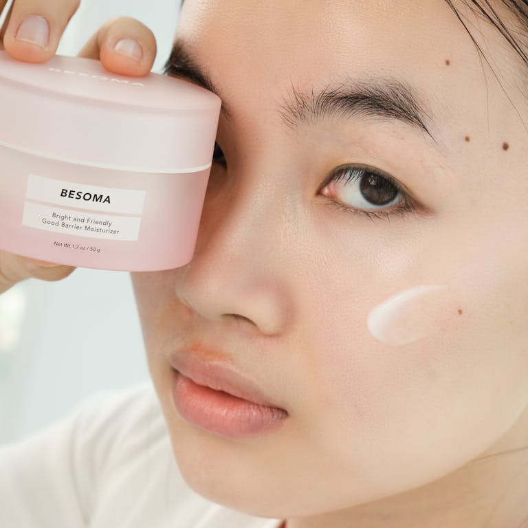 Close-up of an Asian woman holding a moisturizing cream, focusing on skincare.