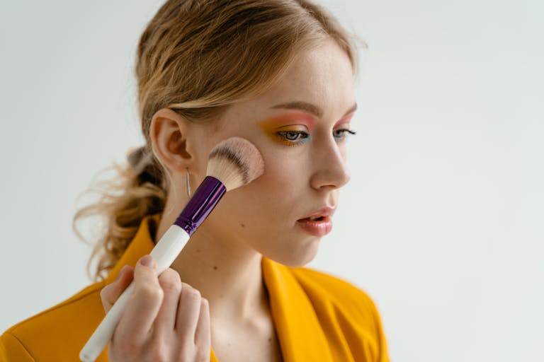 Woman using a makeup brush to apply blush, showcasing beauty and cosmetics indoors.
