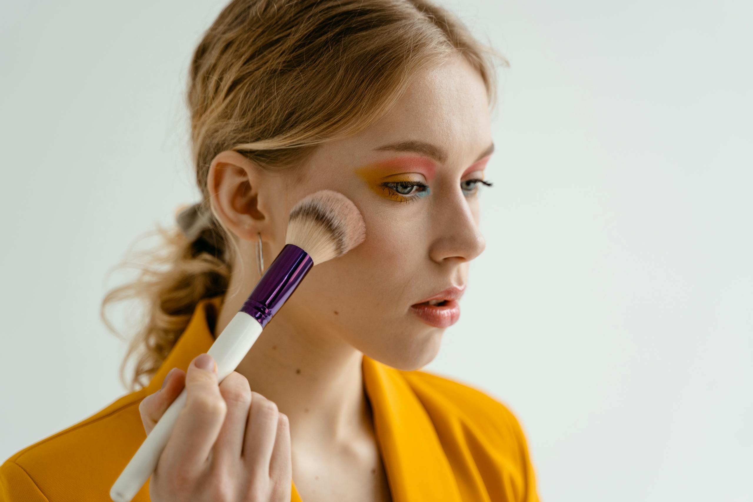 Woman using a makeup brush to apply blush, showcasing beauty and cosmetics indoors.