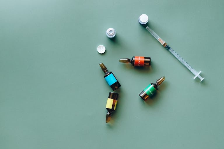 Flat lay of medical ampoules and syringe on a green background, ideal for healthcare themes.