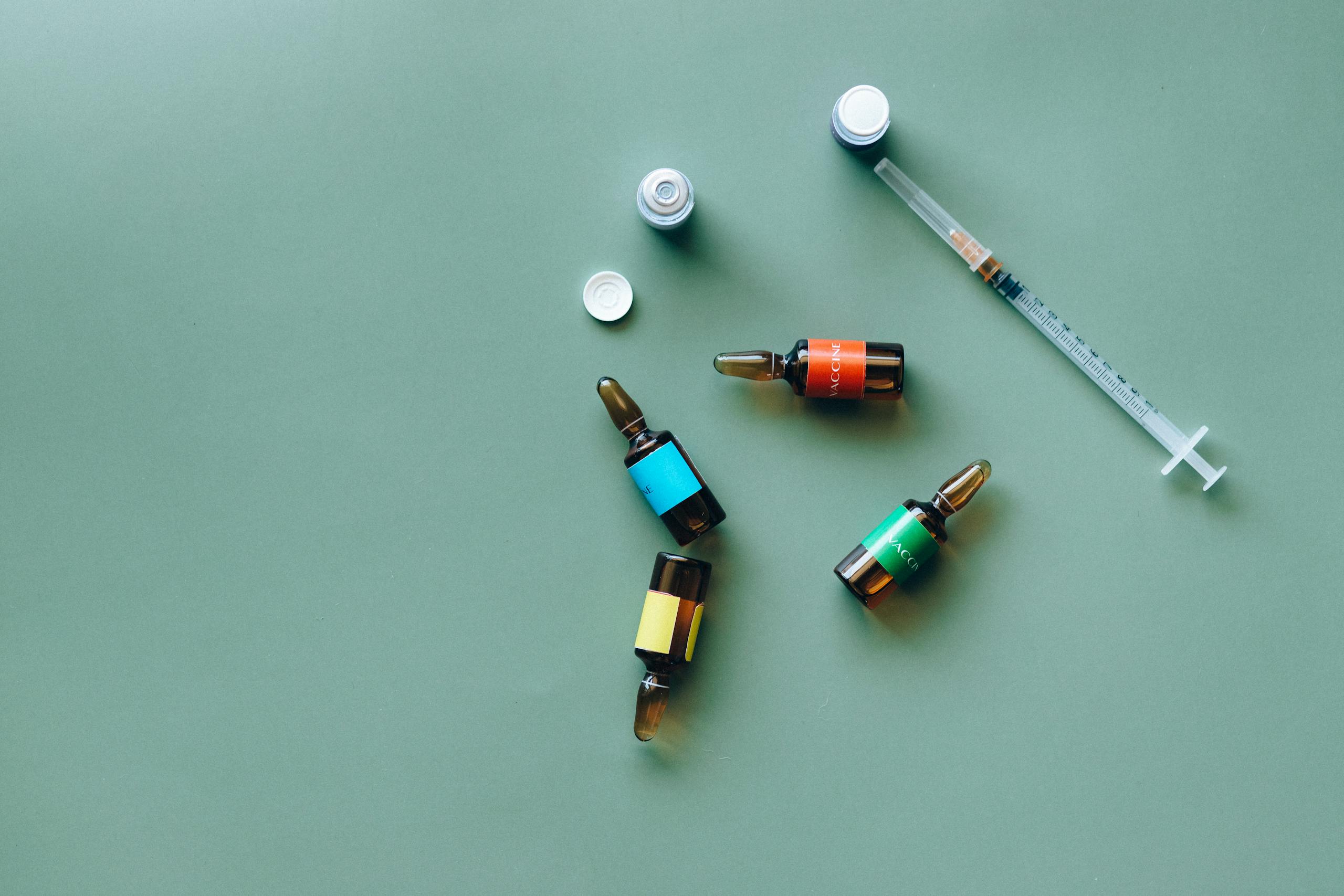 Flat lay of medical ampoules and syringe on a green background, ideal for healthcare themes.